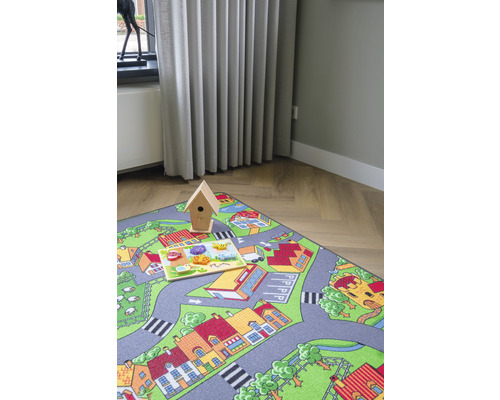 Speelkleed met stratenpatroon, houten vogelhuisje en houten puzzel op de vloer.