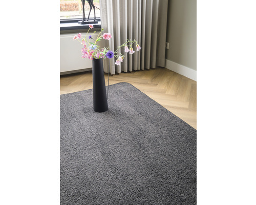 Grijs vloerkleed in woonkamer met een vaas met bloemen op het vloerkleed.