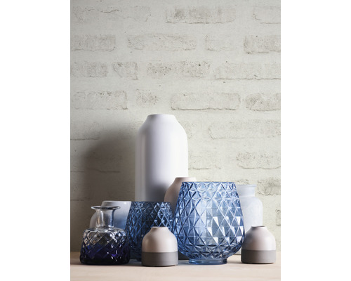 Decoratieve vazen van glas en keramiek op een tafel voor een bakstenen muur