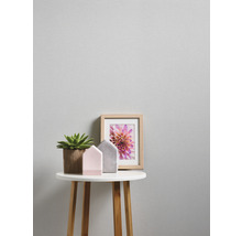 Close-up van een bijzettafel met kamerplant, decoratieve huisjes en fotolijst tegen een gestructureerd behang.