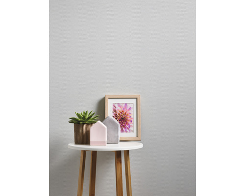 Close-up van een bijzettafel met kamerplant, decoratieve huisjes en fotolijst tegen een gestructureerd behang.