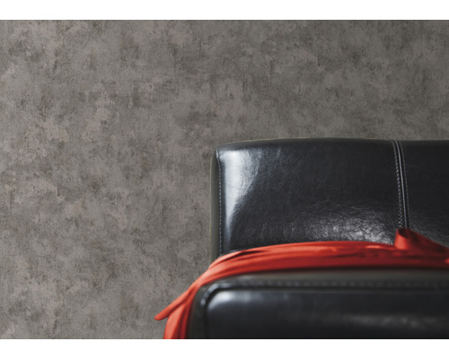 Behang in betonlook naast een zwarte lederen fauteuil