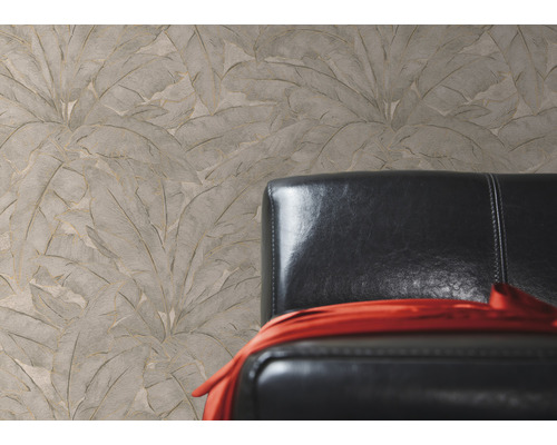 Beige structuurbehang met bladerpatroon naast een zwarte leren fauteuil