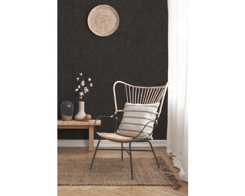 Inrichtingsscène met een fauteuil, een tafeltje, een vaas en een decoratief bord aan een donkere wand.