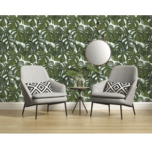 Woonkamer met Monstera-behang, twee grijze fauteuils, kussens met print, ronde spiegel en bijzettafel.