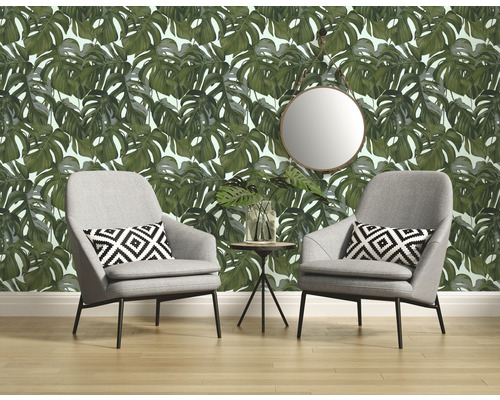 Woonkamer met Monstera-behang, twee grijze fauteuils, kussens met print, ronde spiegel en bijzettafel.