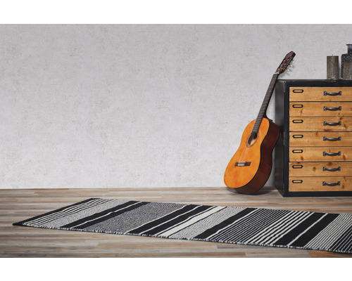 Een kamer met een gestreept vloerkleed, een gitaar en een commode.