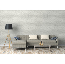 Woonkamer met grijze bank, staande lamp en salontafel voor een bakstenen muur