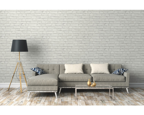 Woonkamer met grijze bank, staande lamp en salontafel voor een bakstenen muur