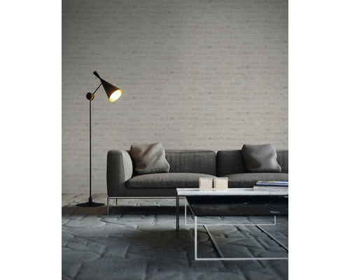 Woonkamer met grijze bank, salontafel en vloerlamp voor een bakstenen muur