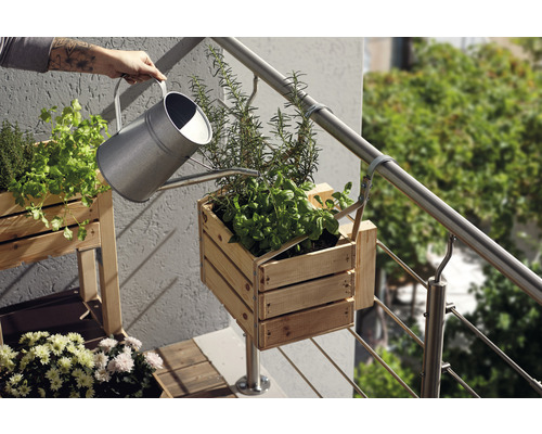 Gieter bij het water geven van kruiden in een houten bak op een balkon.