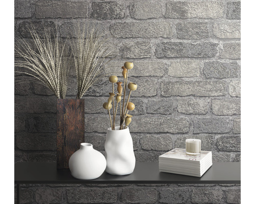 Decoratieve scène met vazen, planten, kaars en stapel boeken tegen een stenen muur.