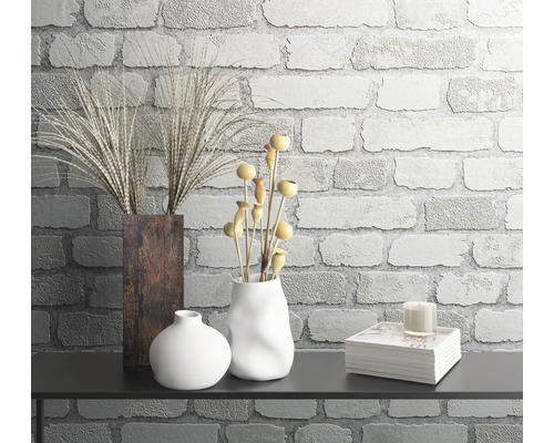 Decoratieve stillevenopstelling met vazen, planten en boeken tegen een bakstenen muur.