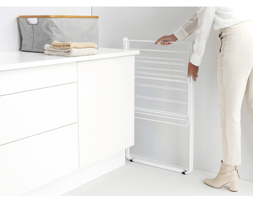 Metalen wasrek wordt door een persoon ingeklapt naast een kast.