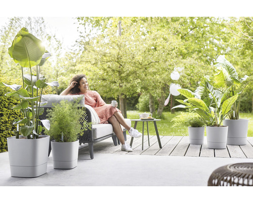 Terrasscène met vrouw op een tuinbank en verschillende planten in bloempotten
