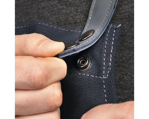 Detailopname van een persoon die een drukknoop bevestigt aan een blauw werkvoorschot.