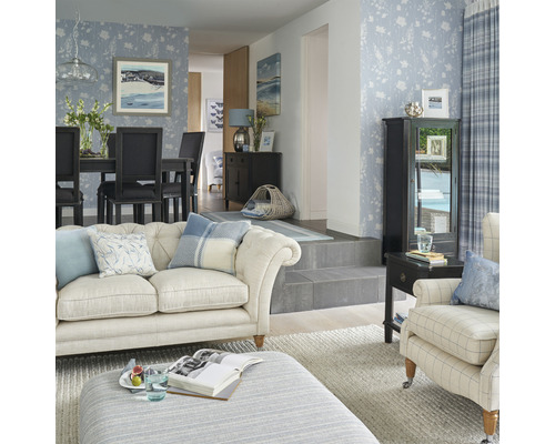 Lichte woonkamer met bloemetjesbehang, bank, fauteuil, eettafel en decoraties