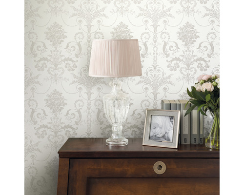 Decoratief interieur met patroonbehang, lamp, fotolijst, boeken en bloemen op een kast.
