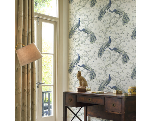 Een werkkamer met een houten bureau, een lamp en behang met een pauwenmotief.