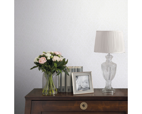 Decoratief behang met een delicaat patroon in een interieur met bloemen, boeken en een lamp op een houten bureau.