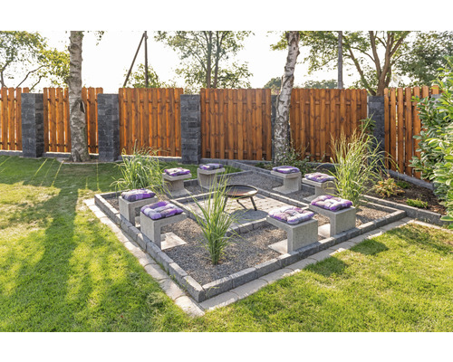 Tuinscene met vuurplaats, zitplaatsen met kussens en houten schutting