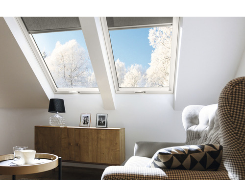 Lichte zolderkamer met dakramen en rolluiken, ingericht met dressoir, lamp en fauteuil