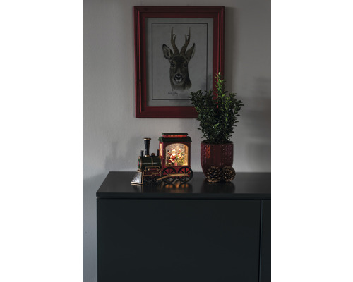 Kerstdecoratie met speelgoedtrein, plant, dennenappels en hertenfoto op een dressoir