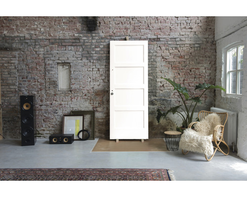 Interieur met een witte binnendeur tegen een bakstenen muur, aangevuld met decoratieve elementen zoals luidsprekers, een fauteuil en een kamerplant