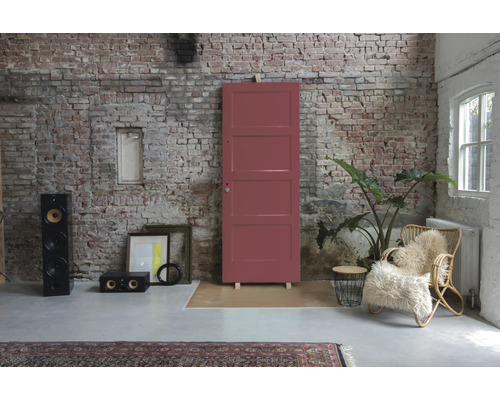 Interieur met rode houten deur tegen een bakstenen muur, aangevuld met luidsprekers, decoraties en een rotan stoel.