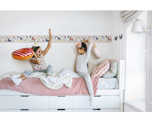 Twee meisjes zitten op een bed met een wit frame en laden voor een wandborder met eenhoornmotief