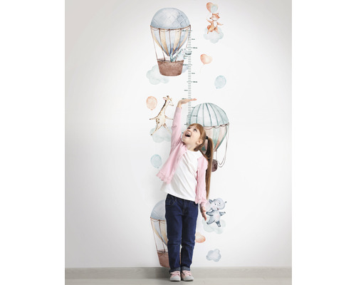 Meisje meet haar lengte met een muursticker-meetlat met heteluchtballon- en dierenmotieven