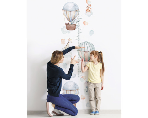 Moeder meet de lengte van een kind met een muursticker meetlat met luchtballonnen en dieren.