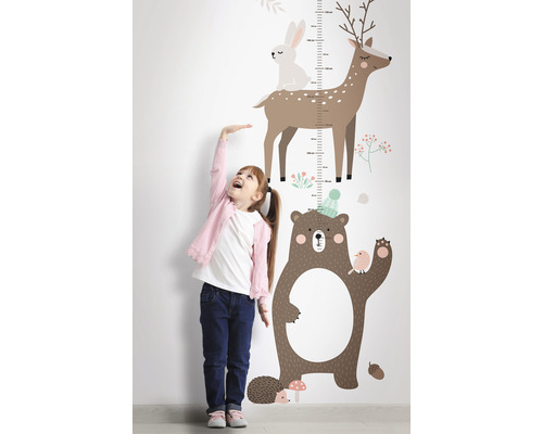 Meisje meet haar lengte naast een muursticker-meetlat met bosdiermotieven.