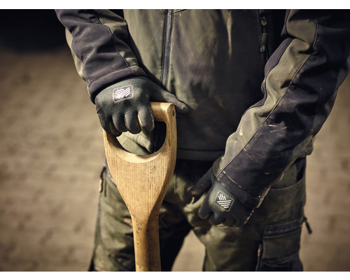 Een persoon in werkkleding houdt een spade met houten handvat vast en draagt werkhandschoenen.