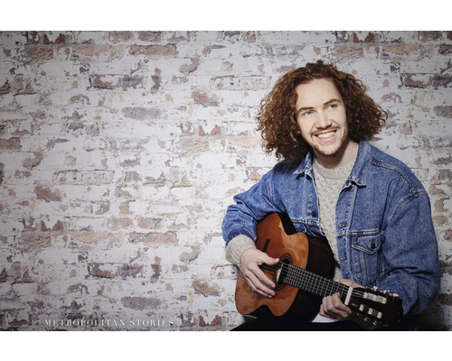 Man met gitaar voor een bakstenen muur