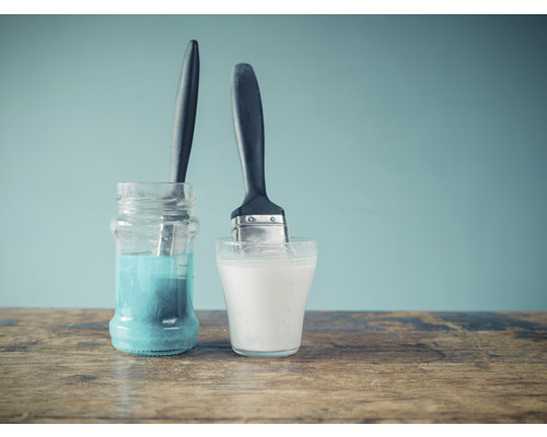 Twee penselen in containers met vloeistof op een houten tafel.