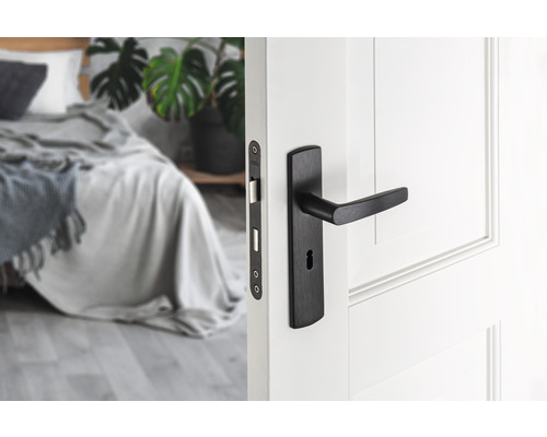 Zwart binnendeurbeslag op een witte deur met zicht op een slaapkamer