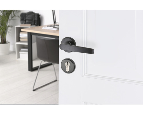 Zwarte deurklink met sleutelrozet op een witte deur in een lichte kamer