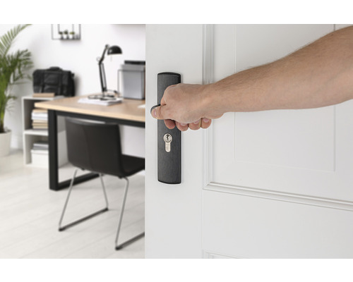 Een hand opent een witte deur met een zwarte deurklink voor een werkkamer.