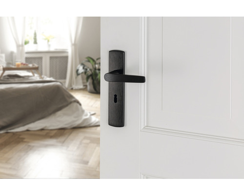 Deurklink met sleutelrozet op een witte deur, slaapkamer op de achtergrond