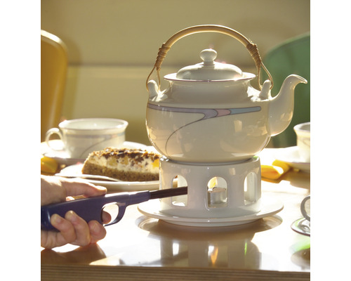 Theepot op een tafel met taart en een persoon die een theelicht aansteekt