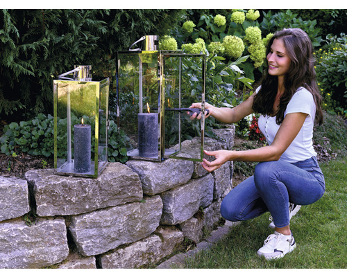 Vrouw steekt kaars aan in windlicht op stenen muur in de tuin