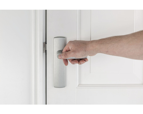 Een hand opent een witte deur met een zilverkleurige deurklink.