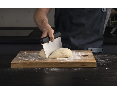Een persoon verdeelt deeg met een deegschraper op een houten plank.