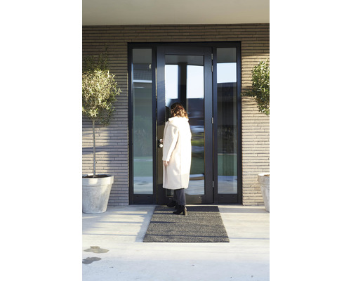 Een vrouw betreedt een huis met een toegangsdeur, een deurmat en plantenbakken.