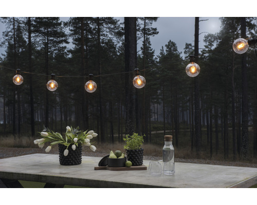 Scene met een lichtsnoer, bloemen en drankjes op een tafel buiten voor een bos