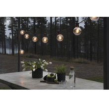 Verlichte lichtslinger boven een tafel buiten met bloemen, planten en drankjes