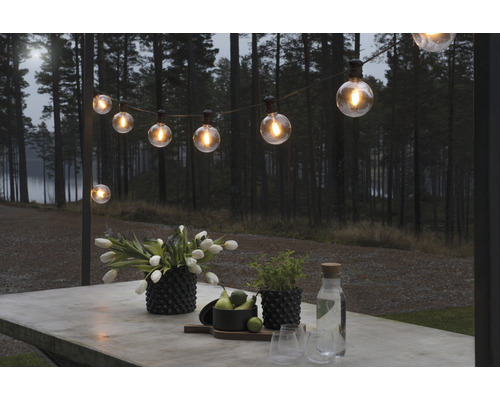 Verlichte lichtslinger boven een tafel buiten met bloemen, planten en drankjes