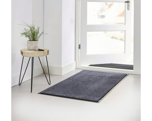 Grijze deurmat voor een open deur en een bijzettafel met een plant