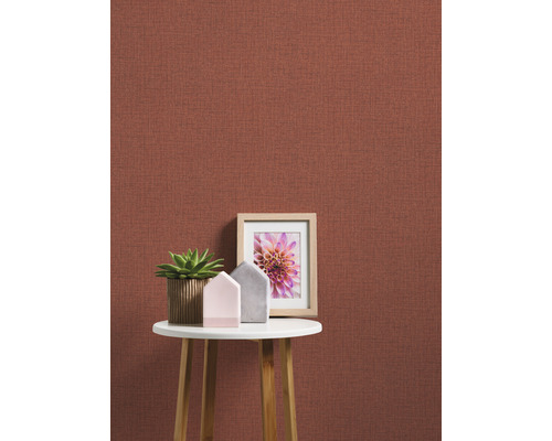 Close-up van een muur met textielbehang, versierd met een tafel, een kamerplant en een fotolijst.